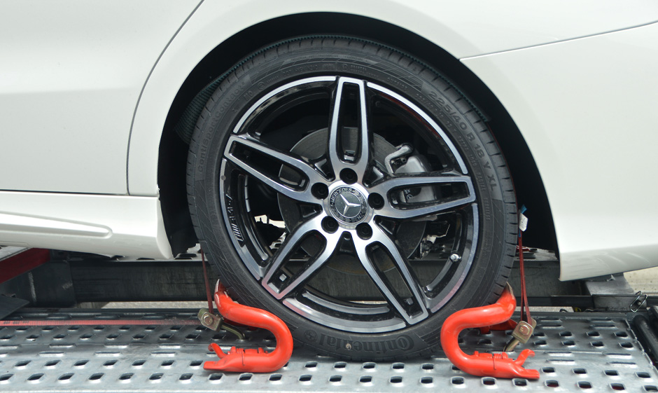 Photo of the wheel of the white car inter-locked in the flatbed towing truck surface Photo of the wheel of the white car inter-locked in the flatbed towing truck surface
